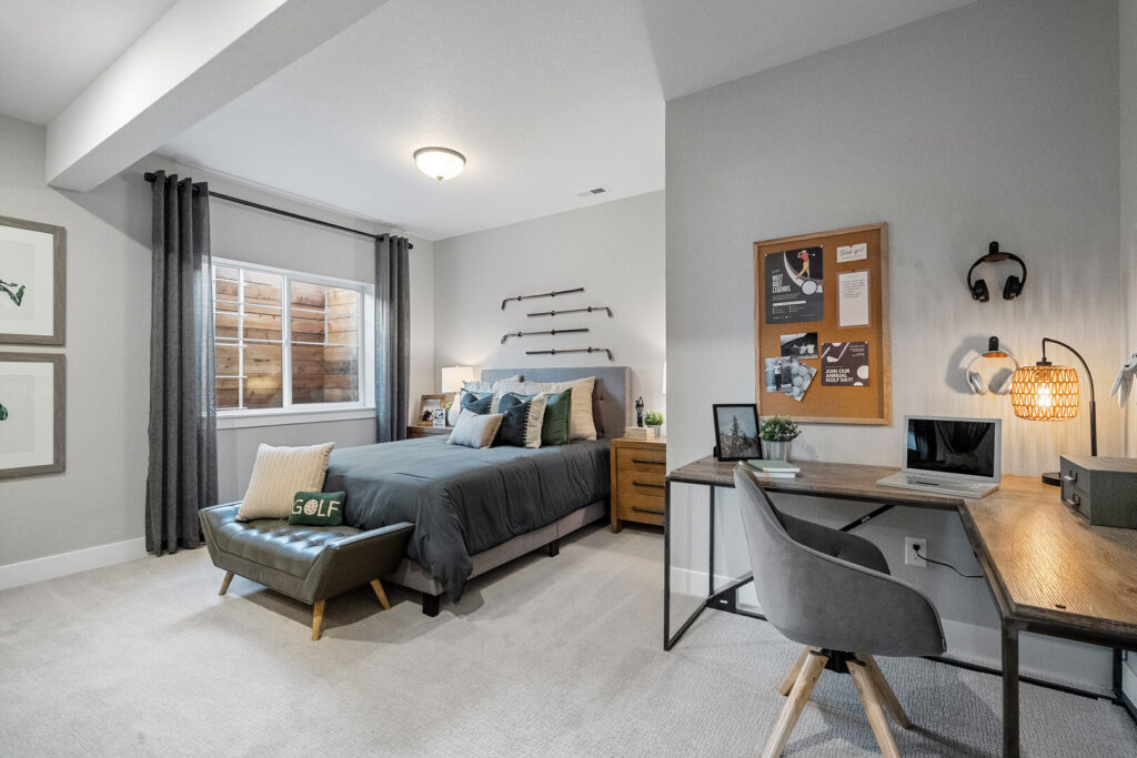 Bedroom with bed, window, curtains, and a desk area with chair and lamp near the wall.