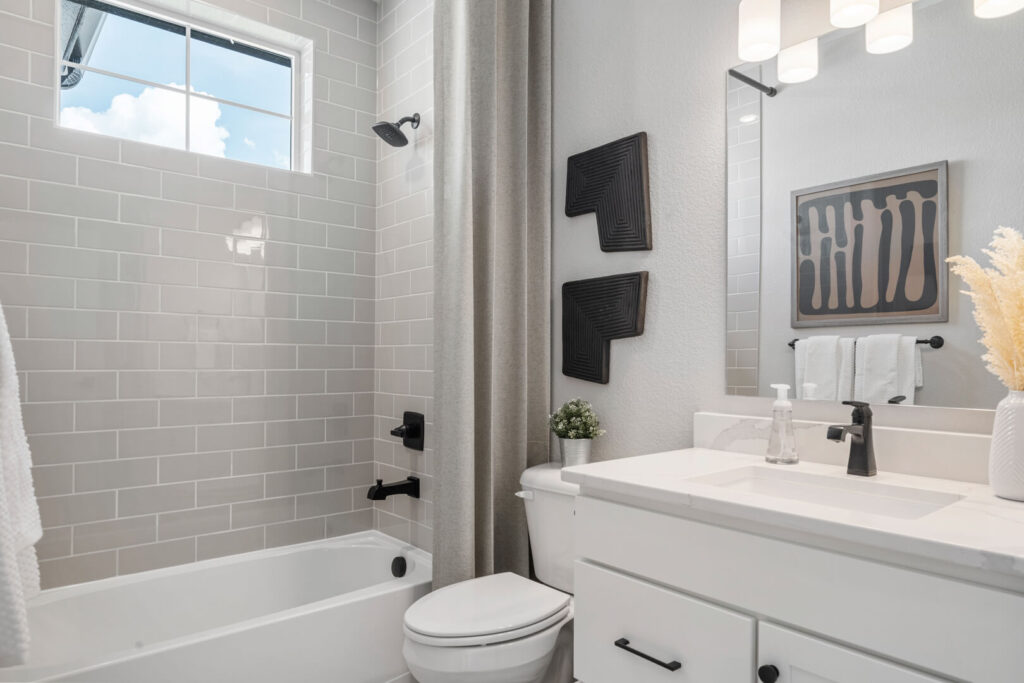 Bathroom with tub-shower, subway tile surround, single-sink vanity, and black fixtures.