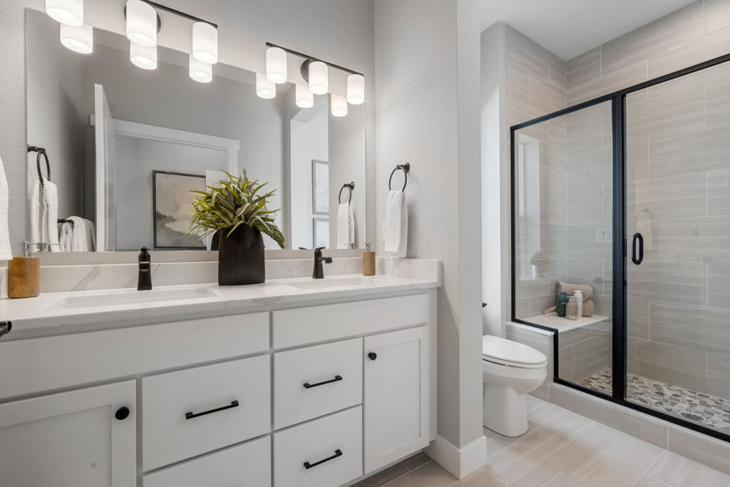 Bright bathroom with double-sink white vanity, black fixtures, and glass-enclosed shower with bench.