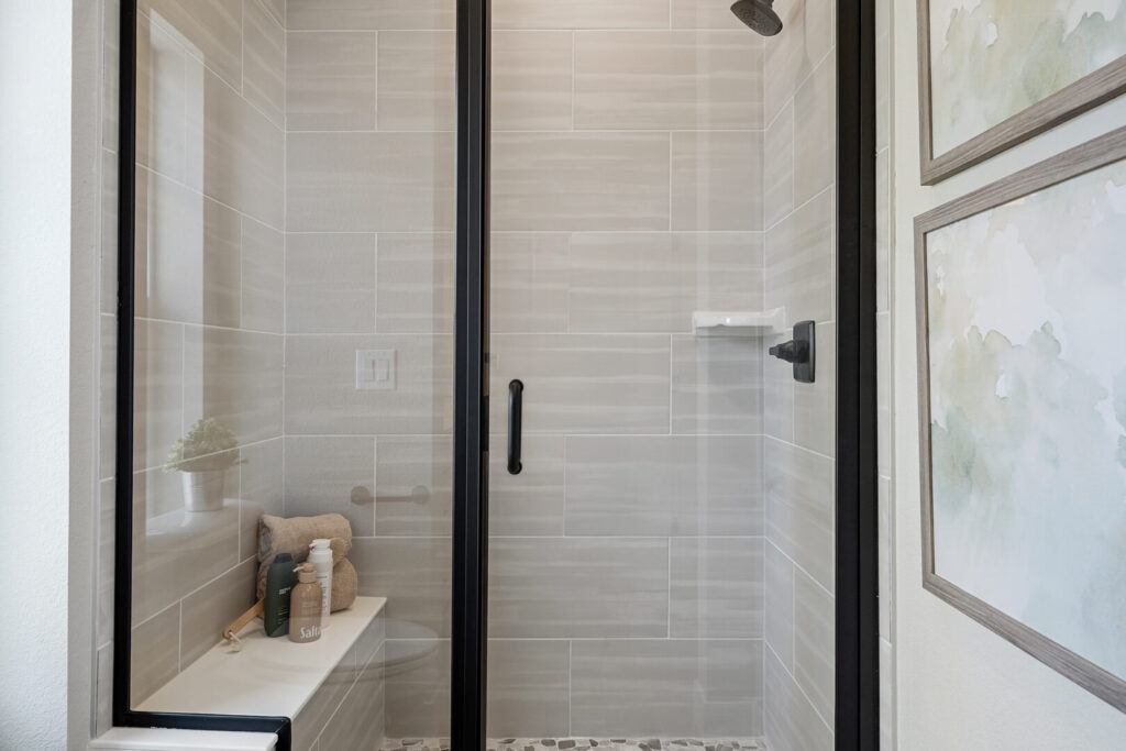Close-up of a tiled shower with black-framed glass door, built-in bench, and pebble floor detail.