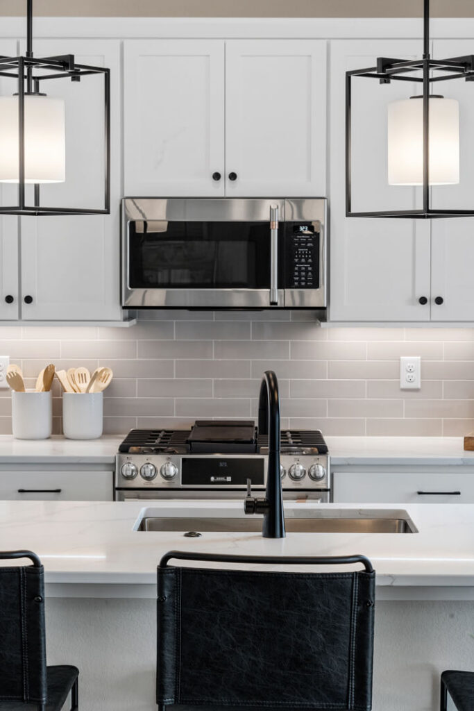 Kitchen island sink and faucet facing a stainless microwave and stove, with pendant lights above.