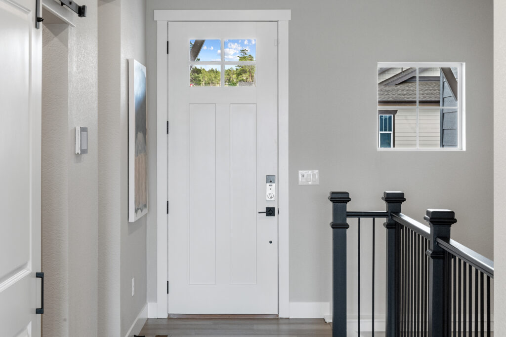 Interior entryway with white front door, small window to the right, and black metal stair railing.