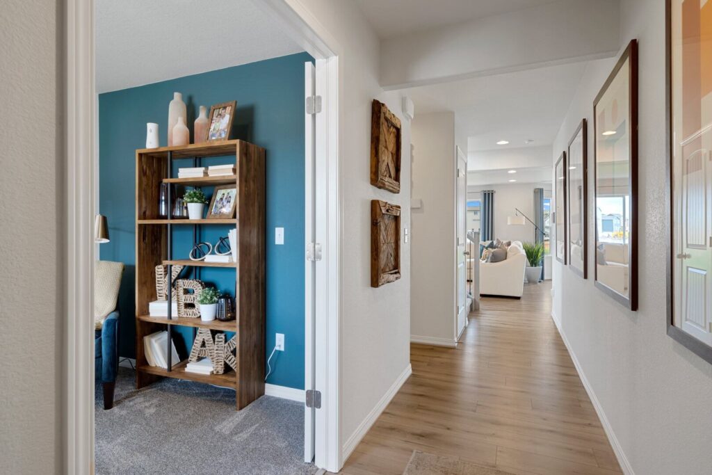 View down a bright hallway with wood-look flooring and an open doorway to a teal-accented office.