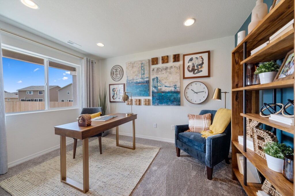 Sunny home office with large window, wooden desk, blue armchair and gallery wall art.