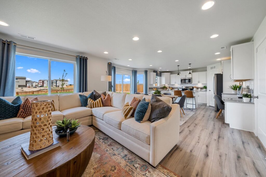 Open living area with large sectional sofa, round wooden coffee table, and wide windows.