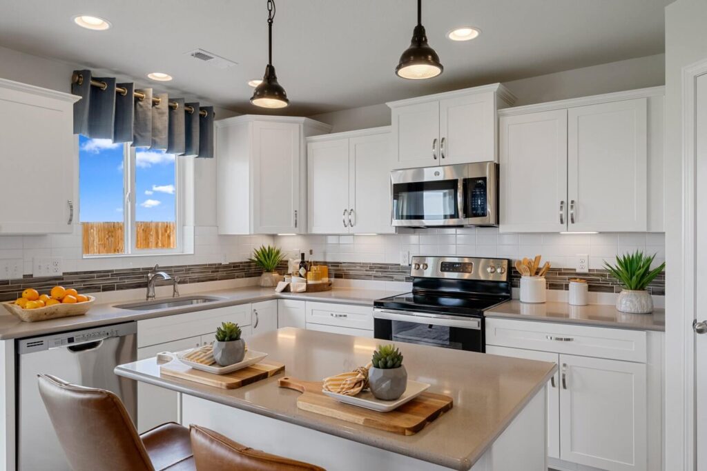 Kitchen sink and stove area with window above sink, island in foreground and pendant lights.