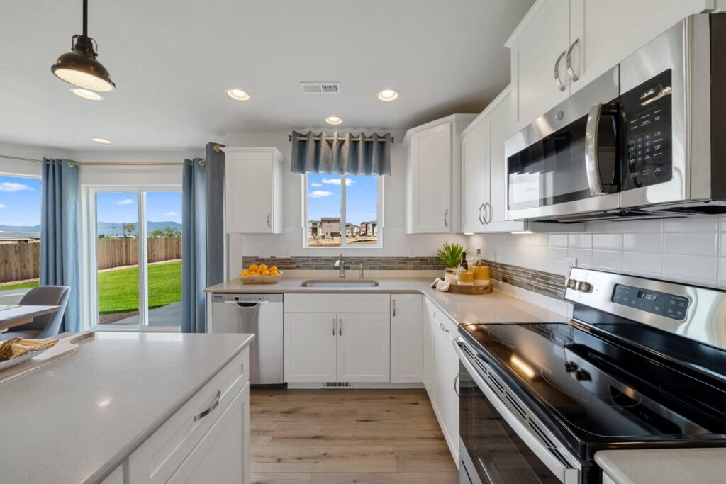 Bright modern kitchen with white cabinets, stainless appliances, and sliding glass doors to a backyard.