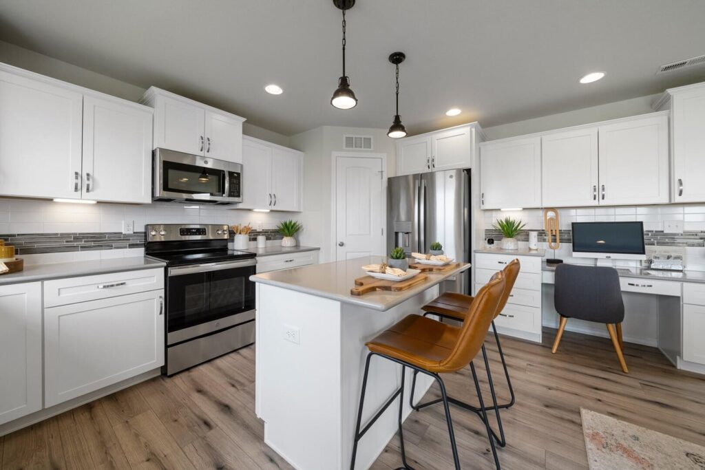 Open kitchen view showing an island with two stools, white cabinetry, and stainless refrigerator.