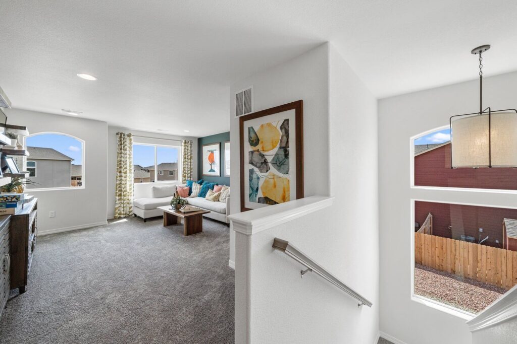 Upper-level landing opening to a carpeted living area with large windows and a stairwell.