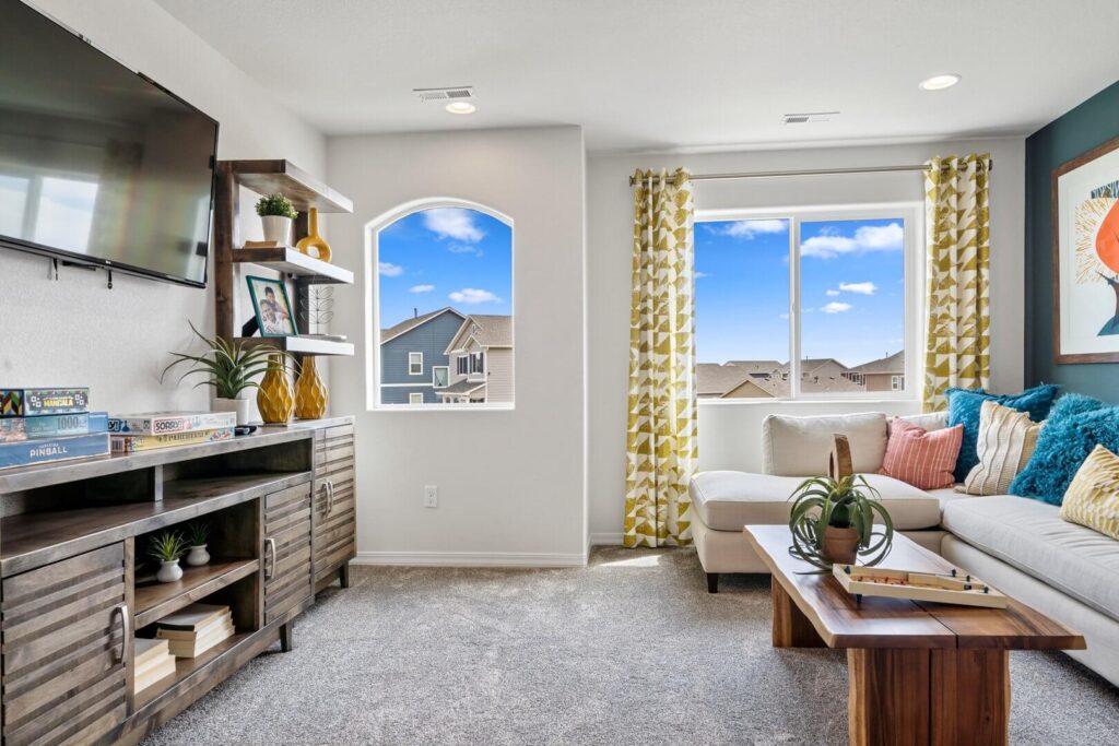 Bright living area with sectional sofa, wooden media console, and two windows with patterned curtains.