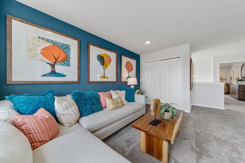 Sitting area with long couch against a blue accent wall and three framed tree prints above.