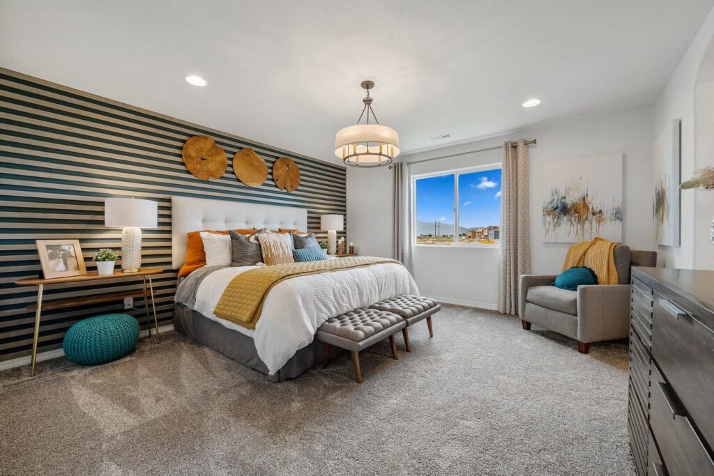 Staged bedroom with striped accent wall, king bed, and ceiling light fixture over carpeted floor.