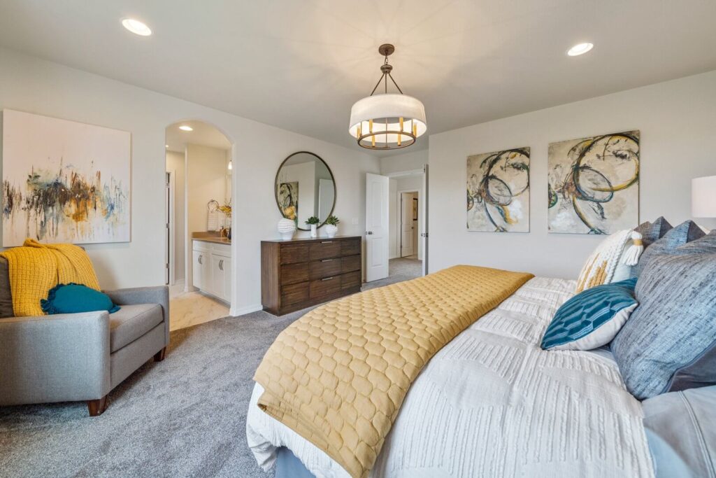 Spacious bedroom with bed, armchair, dresser, wall art, and hanging light fixture.