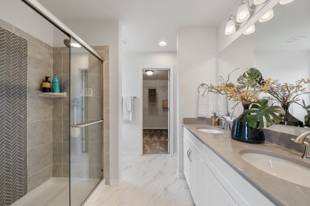 Bathroom with glass-enclosed shower, herringbone tile accent, and double sink vanity.