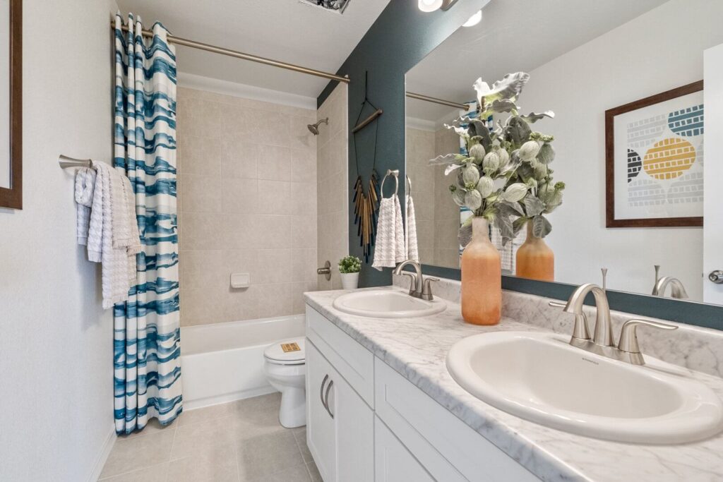 Tile bathtub-shower with blue patterned curtain and dual-sink marble-look vanity.