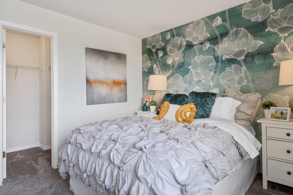 Bedroom with bold botanical wallpaper behind bed, bedside tables and open closet door.