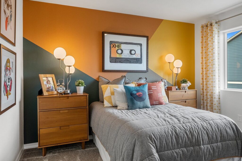 Close view of bed against a colorful diagonal-accent wall with bedside lamps and framed cassette art.