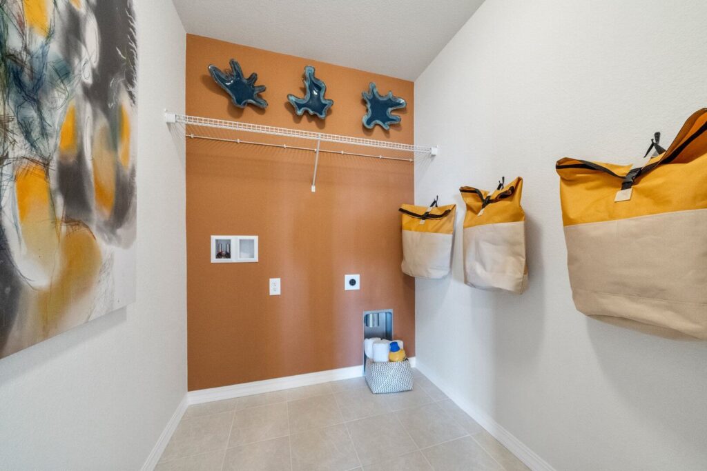 Laundry room with orange feature wall, wall-mounted shelving, and canvas storage bags.