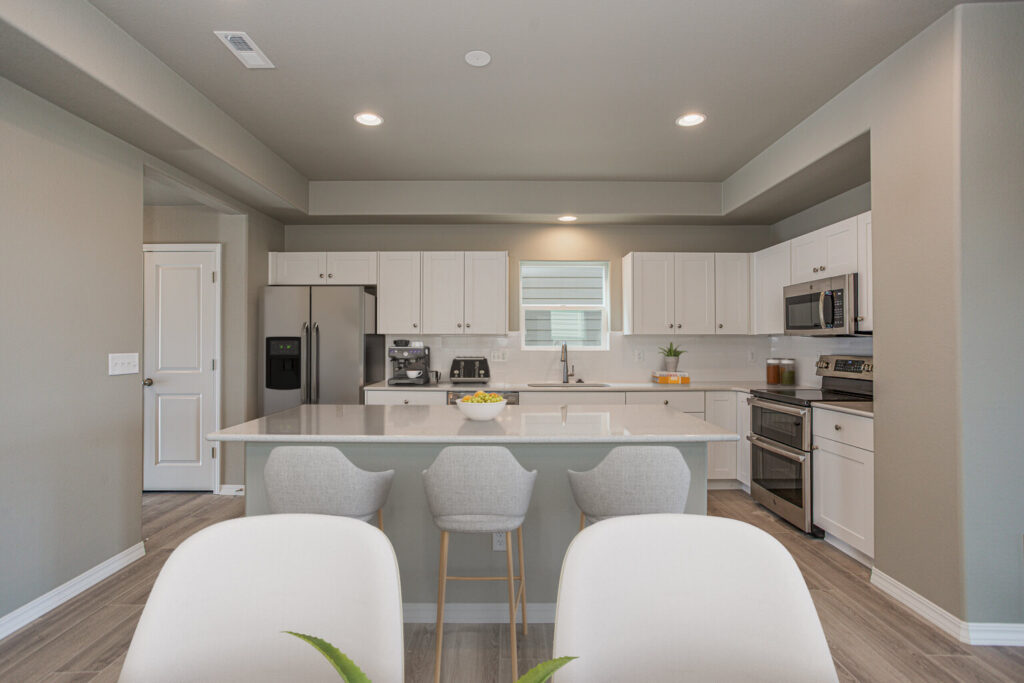 Bright open kitchen with center island, three bar stools, stainless appliances and white cabinets.
