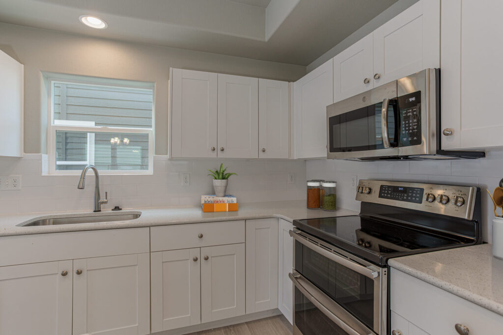 Corner view of a white kitchen with stainless microwave and double oven range under cabinet.