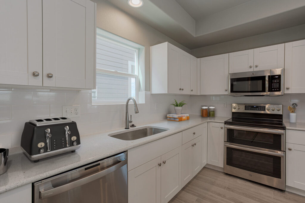Kitchen sink area with dishwasher, toaster, white cabinets and stainless oven to the right.