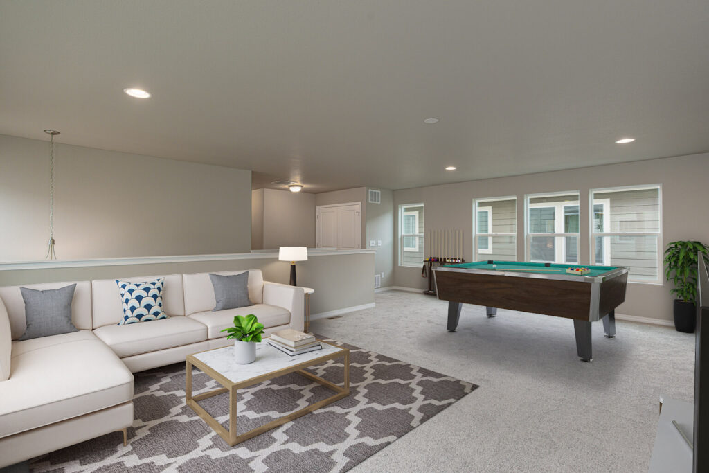 Large carpeted rec room with sectional sofa, coffee table and pool table by windows.