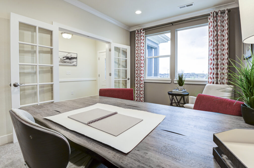 Desk-level perspective toward a window with patterned curtains, French doors, and a small side table.