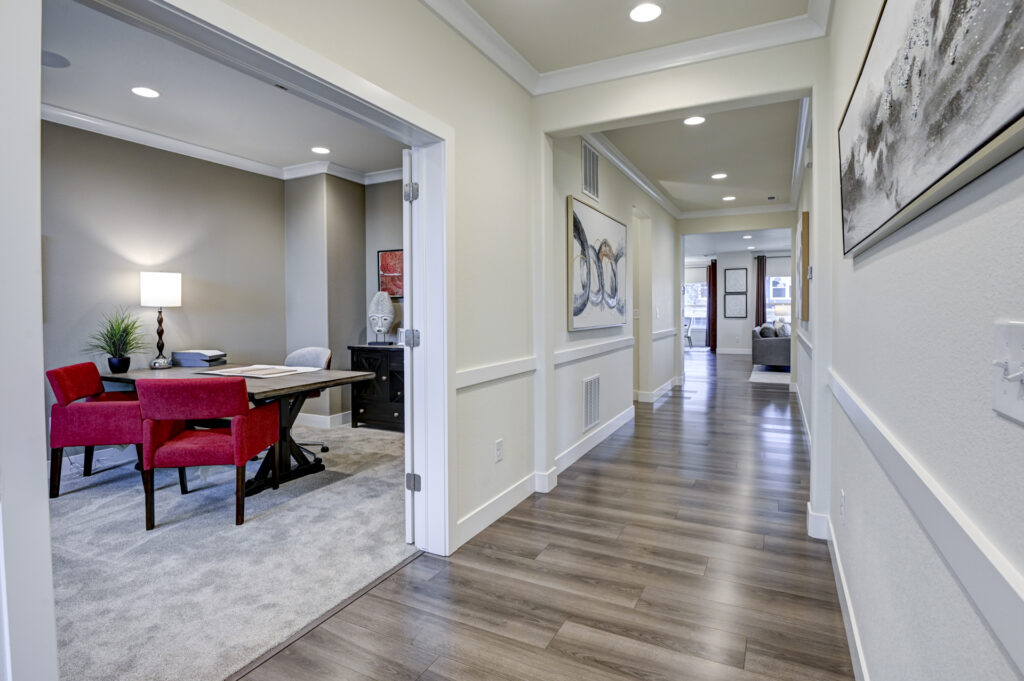 Bright hallway with wood-look flooring and an adjacent office with red chairs and a desk.