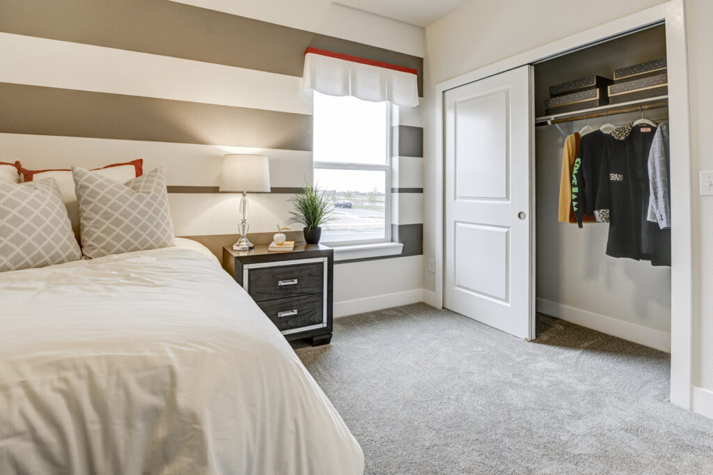 Corner of a bedroom showing nightstand, window and an open closet with hanging clothes.