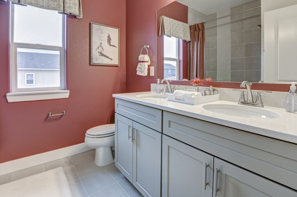 Bathroom with double sink vanity, red painted walls, and a toilet under a window.