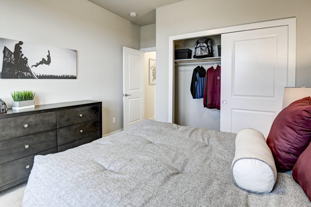 View from bed toward a dresser and open closet with hanging jackets and sliding doors.