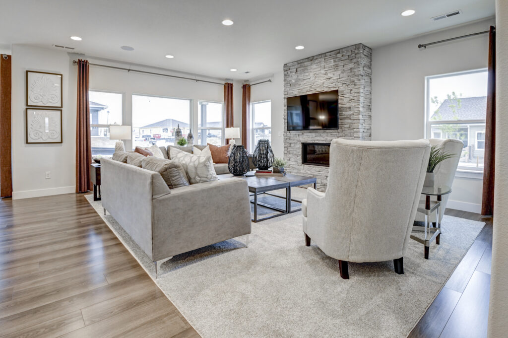 Open living room with sectional sofa, accent chair, large windows and stacked-stone fireplace wall.