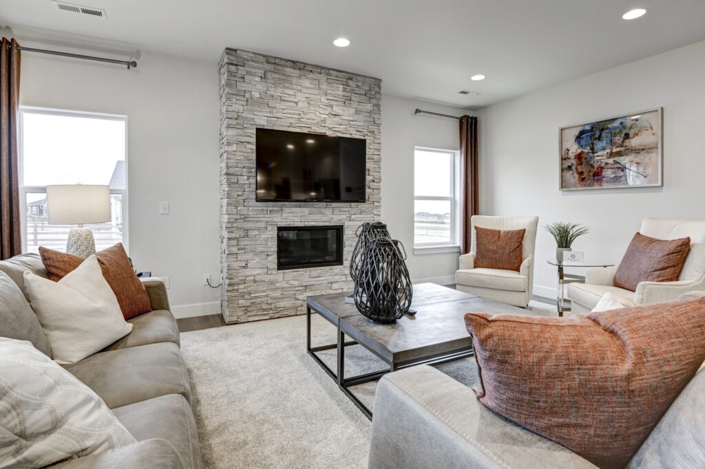 Cozy sitting area facing a stone-clad fireplace with wall-mounted TV and two armchairs.