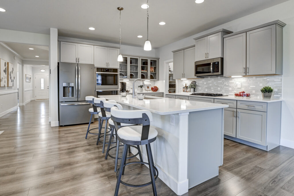 Modern kitchen island with four barstools, pendant lights, and stainless-steel refrigerator.
