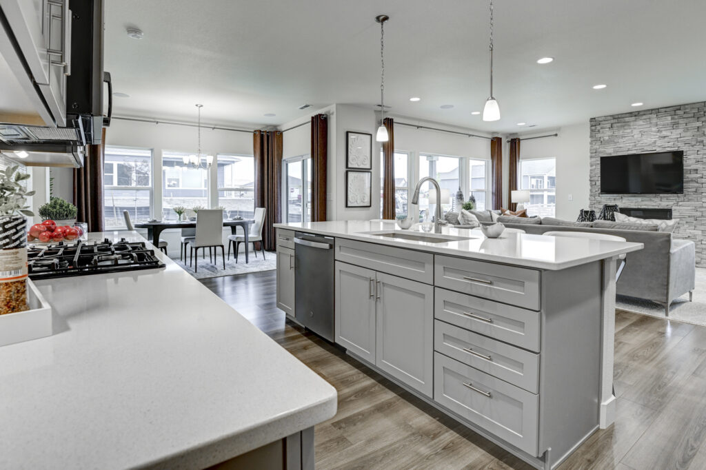 Open-plan kitchen with a large island, gray cabinetry, and adjoining living area with stone fireplace.
