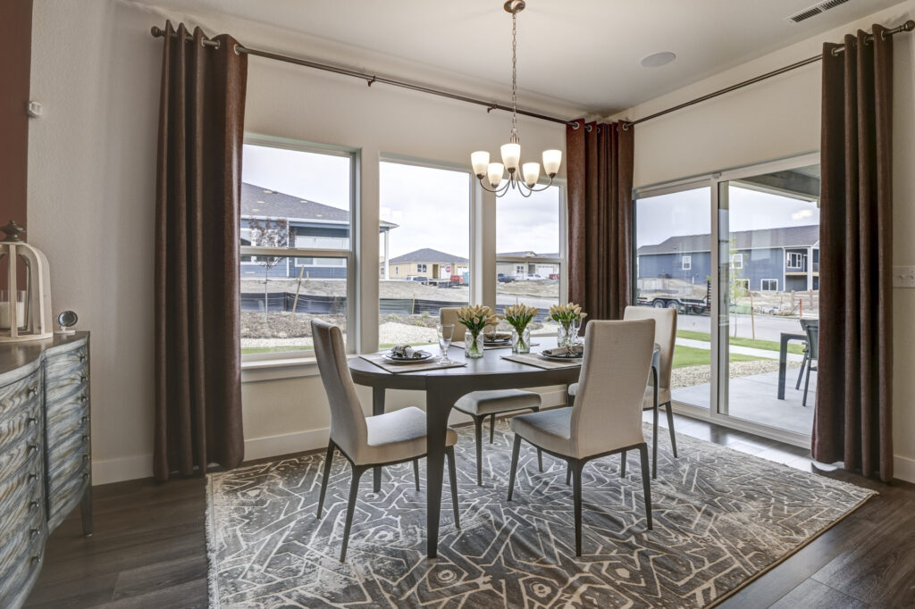 Dining area with a rectangular table, four chairs, patterned rug, and large windows with curtains.