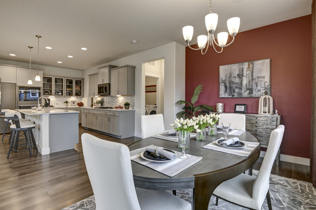 Open dining area with round table, white upholstered chairs, and kitchen in background.
