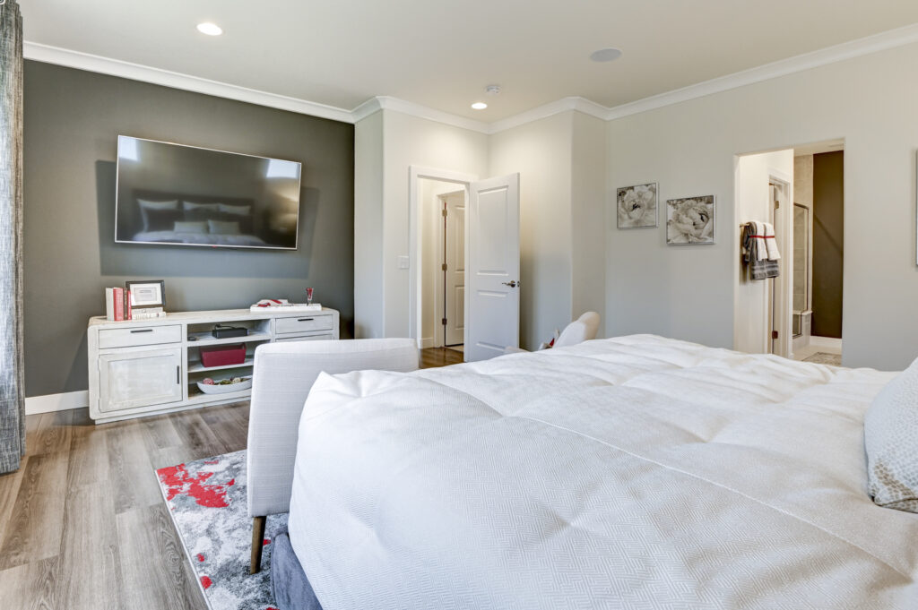 Bedroom view toward media wall with mounted TV and white console, bed in foreground.