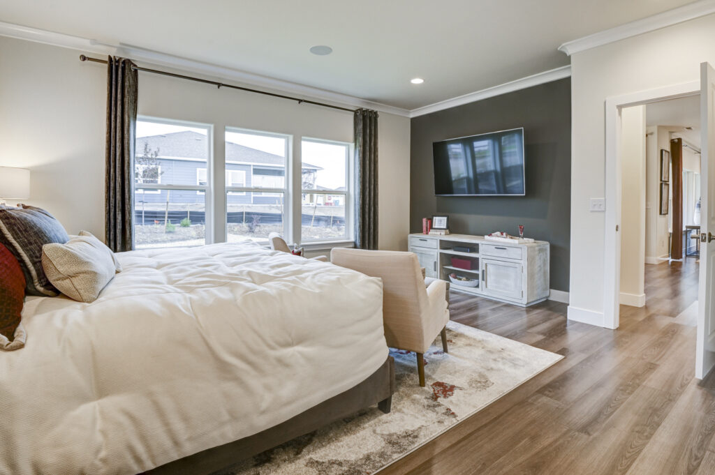 Bedroom with large windows, bed facing TV wall, and curtains framing exterior view.