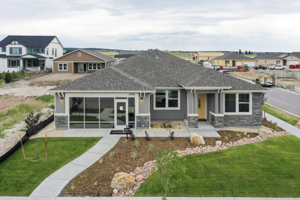Photograph of a single-story gray house with stone accents, yellow front door and landscaped yard.