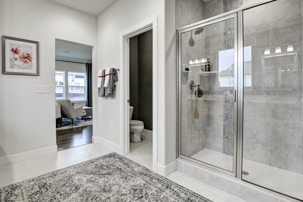 Bathroom view with glass-enclosed tiled shower, doorway to toilet, and open entry to another room.