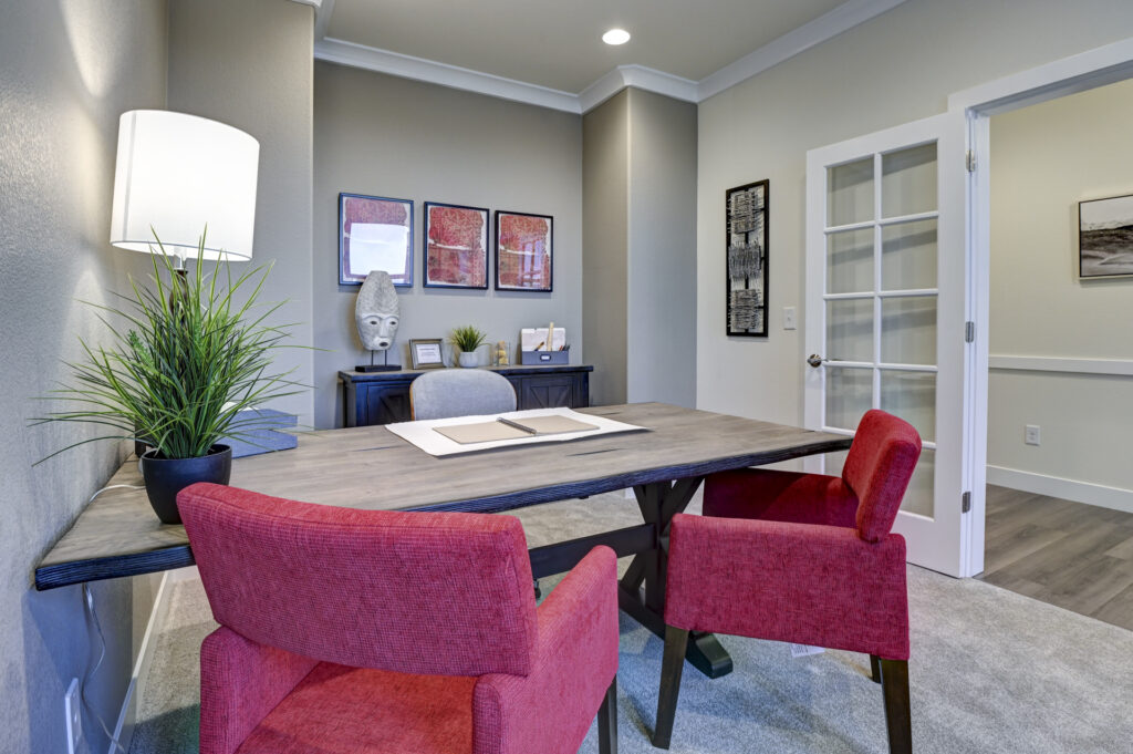 Desk-focused view of an office with red chairs, a lamp, potted plant, and a glass-paneled door.