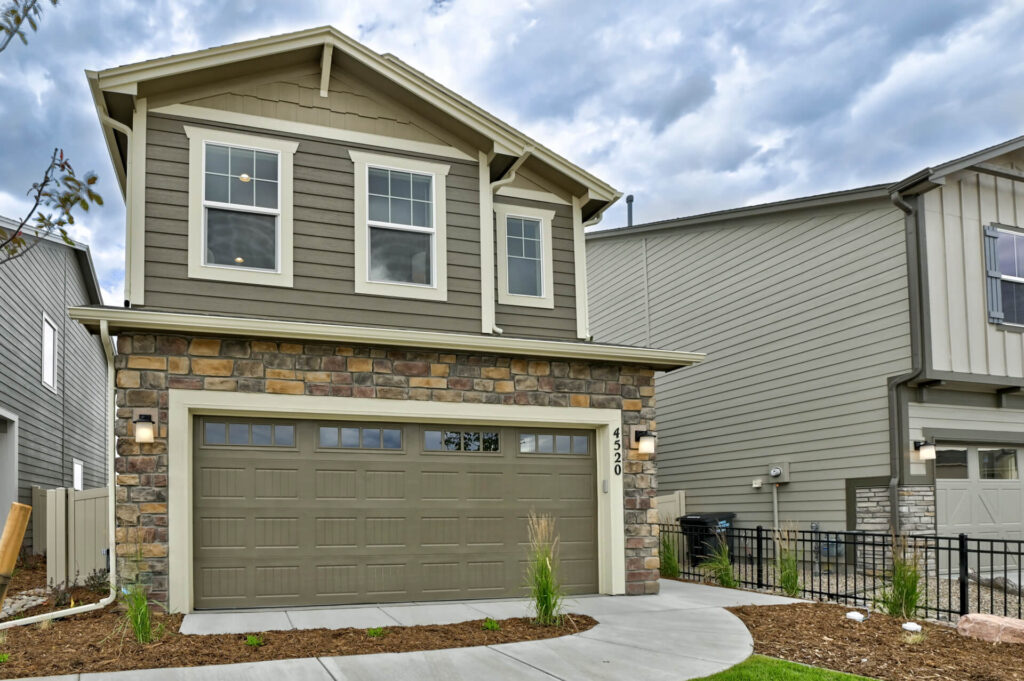 Photograph of a two-story home with stone veneer base, upper siding, and a closed two-car garage.