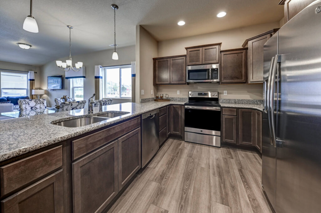 Open kitchen with granite island, double-basin sink, pendant lights, and stainless appliances.