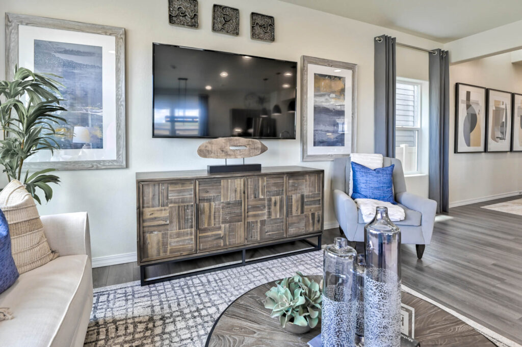 Wall-mounted TV above a wooden media cabinet, flanked by framed artwork and a chair.