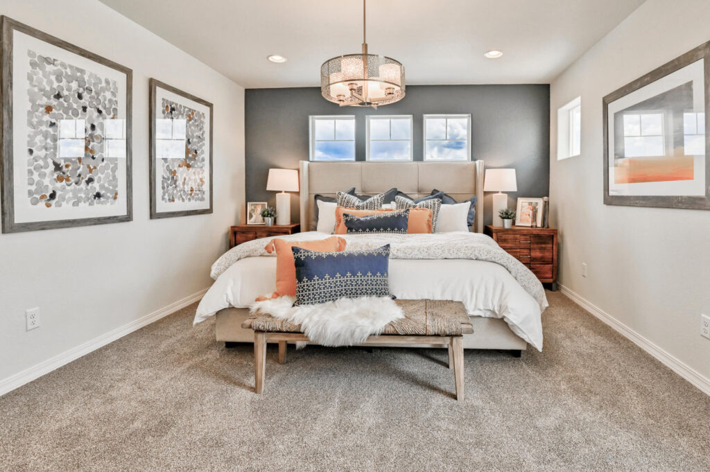 Bedroom with upholstered bed, layered pillows, bench at foot, and three small windows above.