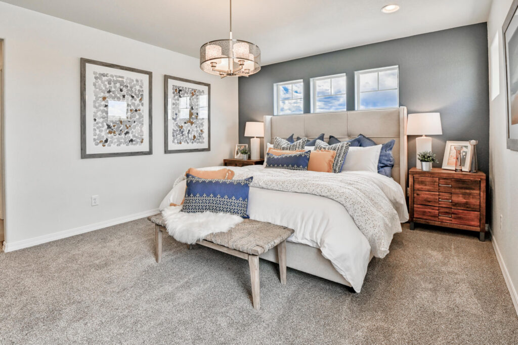 Staged bedroom with upholstered headboard, bench, decorative pillows and framed wall art.