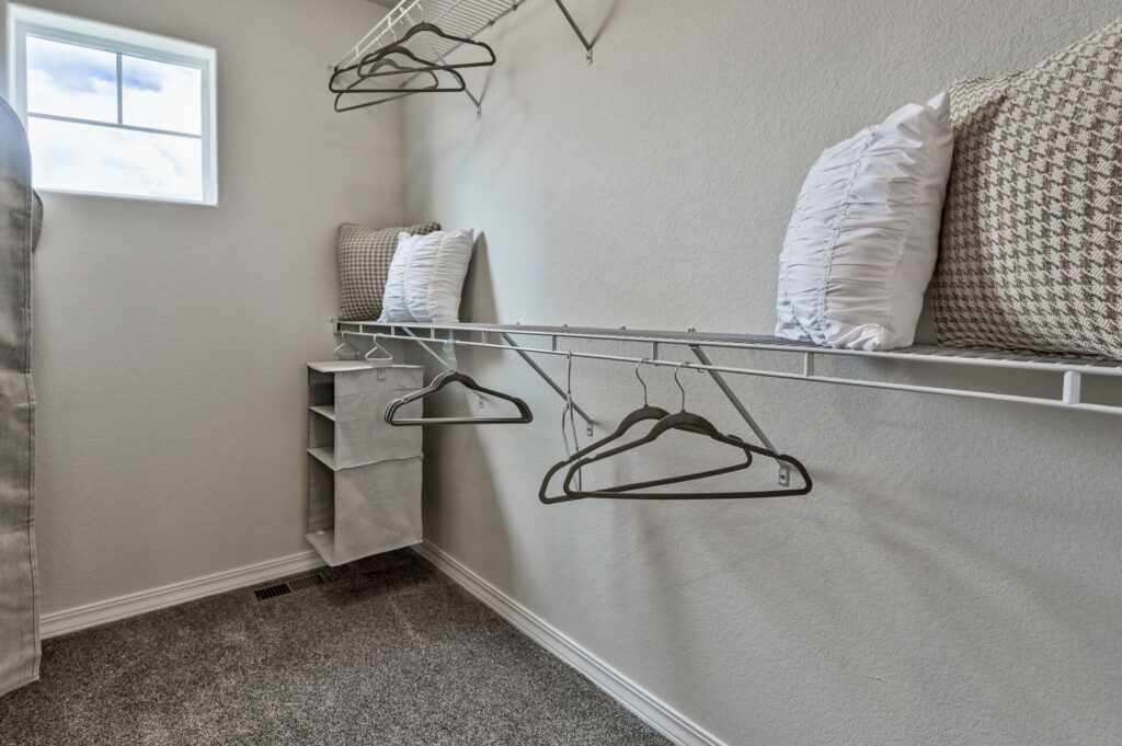 Small walk-in closet with wire shelving, a few hangers, fabric organizer and decorative pillows.