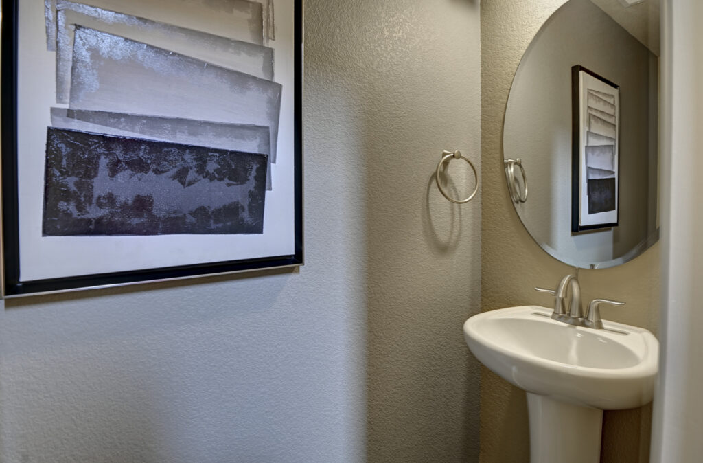 Small powder room with pedestal sink, round mirror, towel ring, and framed abstract art.