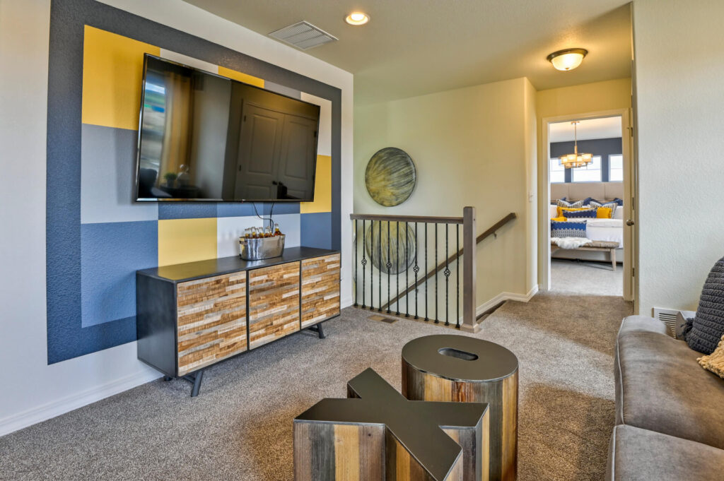 Media wall with mounted flat-screen TV, wooden console and decorative painted accent square behind TV.